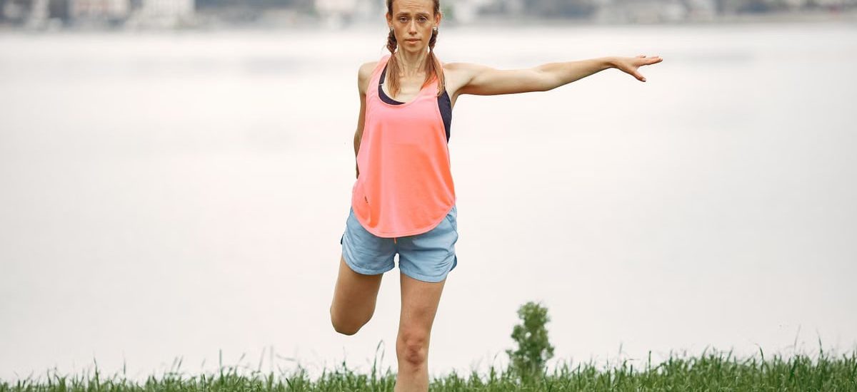 Woman exercising and stretching by a lakeside in a peaceful outdoor setting.