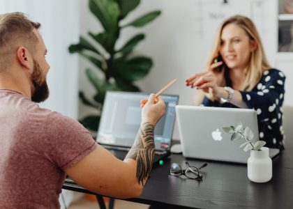 Man and woman discussing work at a table with laptops in a modern office.